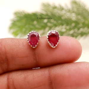 Puede incluir: Un par de pendientes de plata con piedras preciosas rojas en forma de pera. Los pendientes están engastados en un diseño simple y elegante.