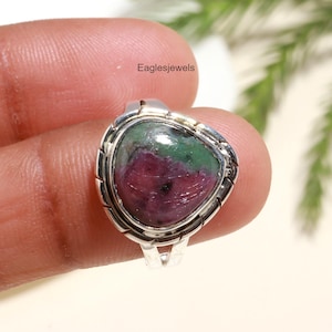 Może przedstawiać: Srebrny pierścionek z trójkątnym zielono-różowym kamieniem szlachetnym. Pierścionek ma ozdobną ramkę wokół kamienia.