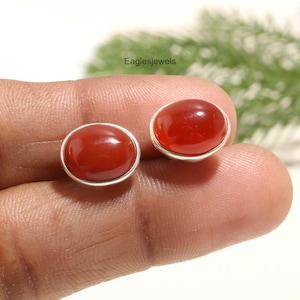 May include: A pair of silver earrings with red carnelian gemstones. The earrings are oval shaped and have a smooth, polished finish.