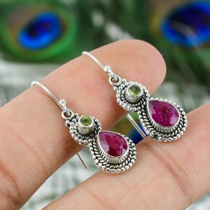 Puede incluir: Pendientes de plata con un rubí en forma de pera y una piedra verde más pequeña. Los pendientes tienen un diseño de plata detallado.