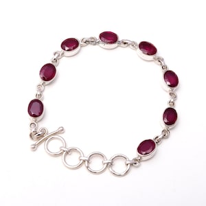 May include: A silver bracelet with a chain link design and oval-shaped red gemstones. The bracelet has a toggle clasp.