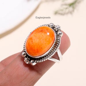 May include: A silver ring with an orange oval gemstone set in a twisted silver band. The ring is adorned with small silver beads around the setting.