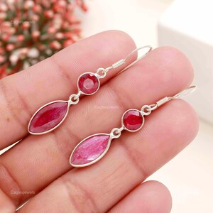 May include: A pair of silver earrings with red ruby gemstones. The earrings feature a teardrop-shaped ruby and a round ruby.