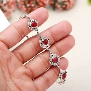 Peut inclure: Un bracelet en argent avec des pierres précieuses rouges serties dans des motifs circulaires. Le bracelet a un design délicat de chaîne à maillons.
