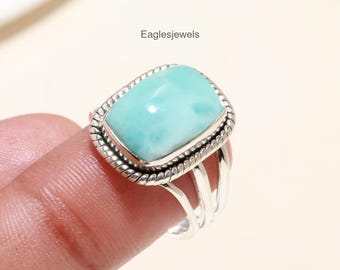 Könnte beinhalten: Ein silberner Ring mit einem rechteckigen, hellblauen Edelstein, der in einer silbernen Fassung sitzt. Der Ring hat ein geflochtenes Band.