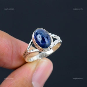 Può includere: Un anello d'argento con una pietra ovale blu. L'anello ha una fascia delicata e attorcigliata.