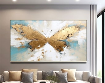 May include: Abstract painting of a gold butterfly on a white and blue background. The butterfly is painted with gold leaf and has a textured surface. The painting is framed in a gold frame.