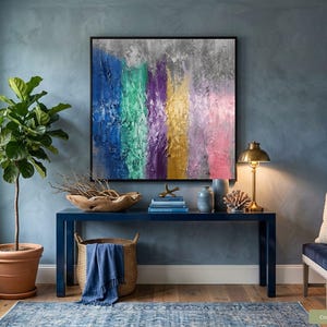 May include: An abstract artwork with vertical stripes of blue, green, purple, yellow, and pink. It hangs above a navy blue console table with a lamp and a wooden bowl. A large potted plant and a blue rug are also visible in the room.