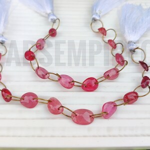 May include: A strand of pink gemstone beads strung on a gold chain with white tassels at each end.