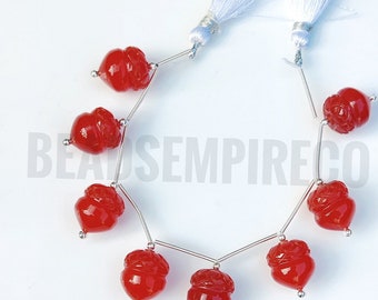 May include: A strand of red carnelian beads with a carved acorn design. The beads are strung on silver wire and have silver caps on the ends. The strand is finished with two white tassels.