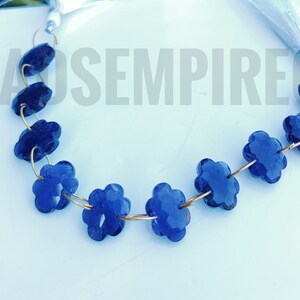 Puede incluir: Una hebra de cuentas de piedras preciosas de color azul oscuro en forma de flor, enhebradas en un alambre dorado.