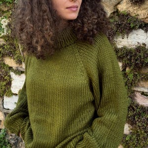 The photo shows a girl in a knitted green sweater. She is standing on a city street.