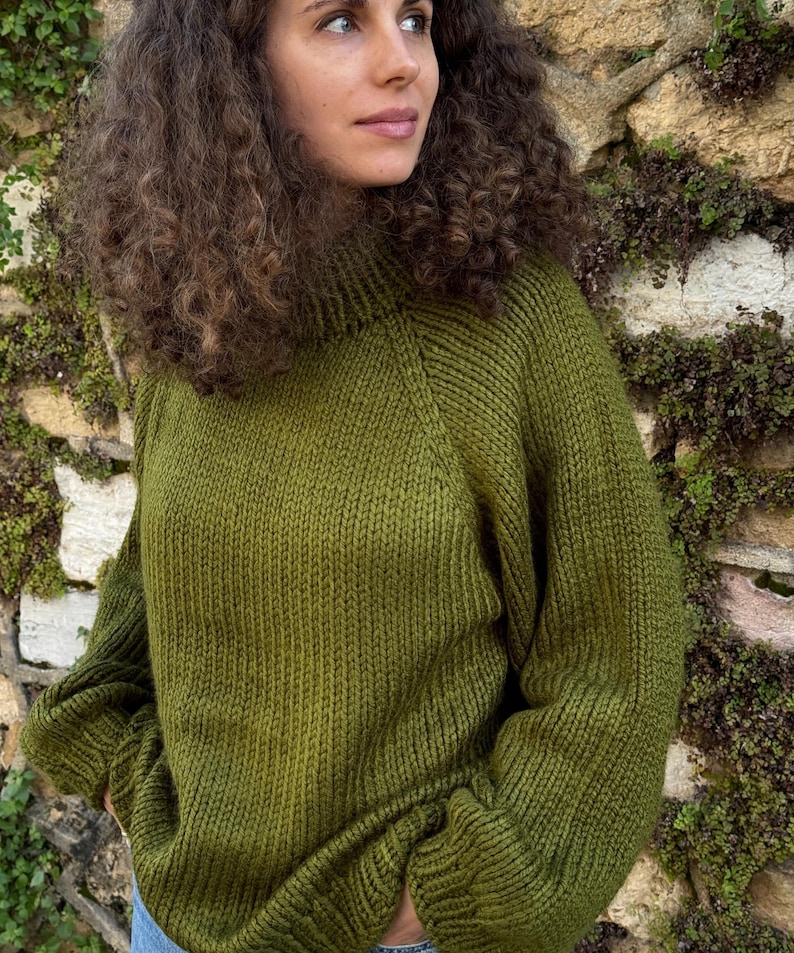 The photo shows a girl in a knitted green sweater. She is standing on a city street.