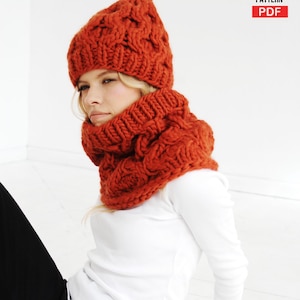 Può includere: Un set di cappello e scaldacollo arancione lavorato a maglia. Il cappello ha un pompon in cima e un design a trecce. Lo scaldacollo è di colore arancione abbinato e presenta un motivo a trecce simile. Il testo "KNITTING PATTERN PDF" è in alto a destra.