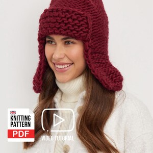 Puede incluir: Un gorro de punto burdeos con orejeras. El gorro está hecho de hilo grueso y tiene un aspecto texturizado. La imagen también incluye un logotipo de "Knitting Pattern PDF" y un icono de "Video Tutorial".