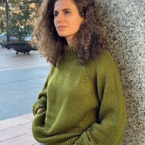 The photo shows a girl in a knitted green sweater. She is standing on a city street.