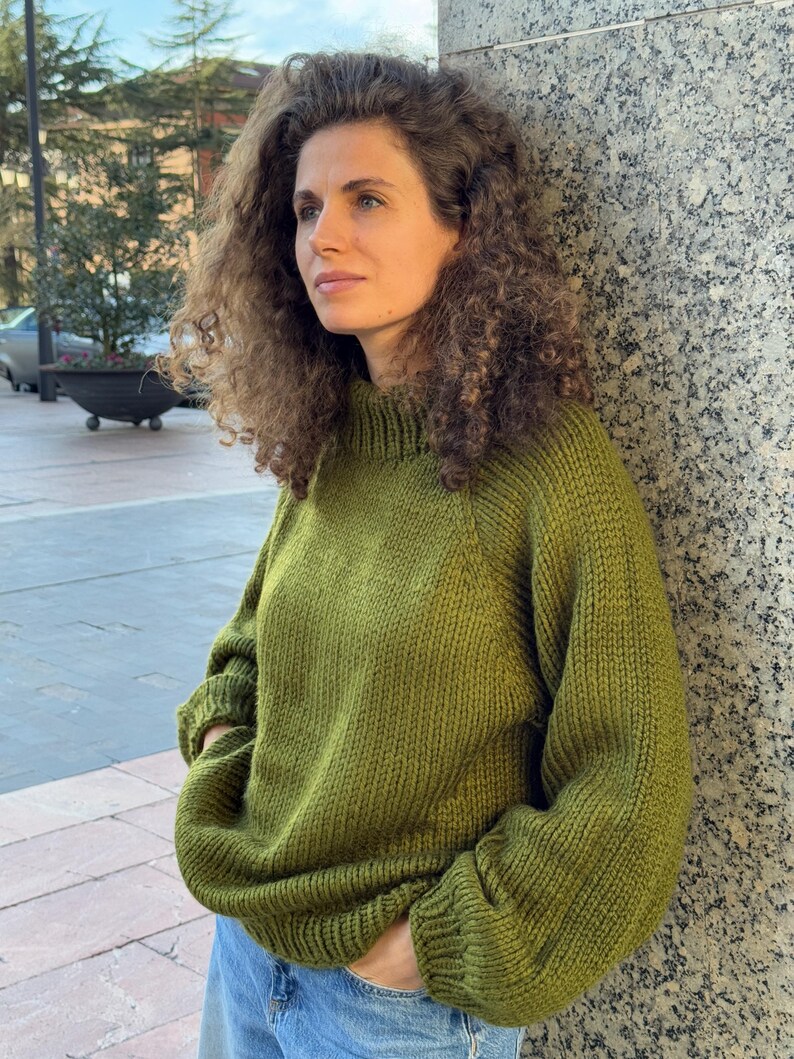 The photo shows a girl in a knitted green sweater. She is standing on a city street.