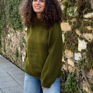 The photo shows a girl in a knitted green sweater. She is standing on a city street.