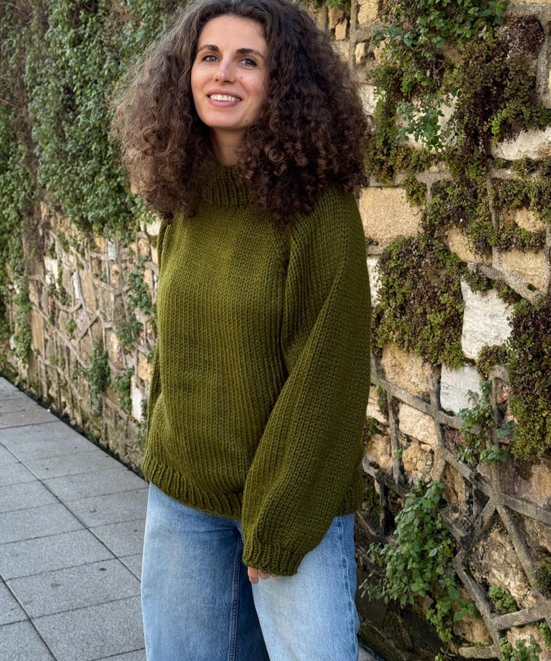 The photo shows a girl in a knitted green sweater. She is standing on a city street.