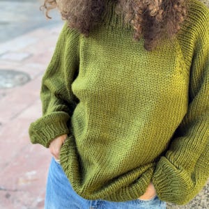 The photo shows a girl in a knitted green sweater. She is standing on a city street.