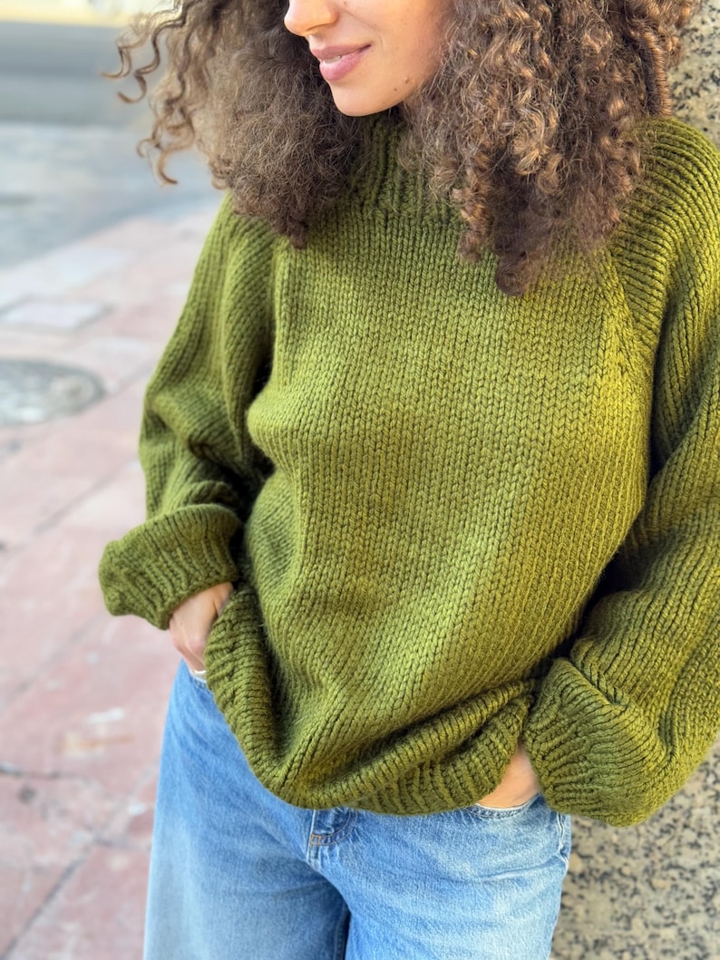 The photo shows a girl in a knitted green sweater. She is standing on a city street.