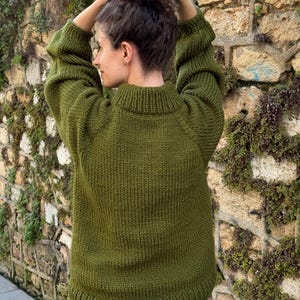 The photo shows a girl in a knitted green sweater. She is standing on a city street.