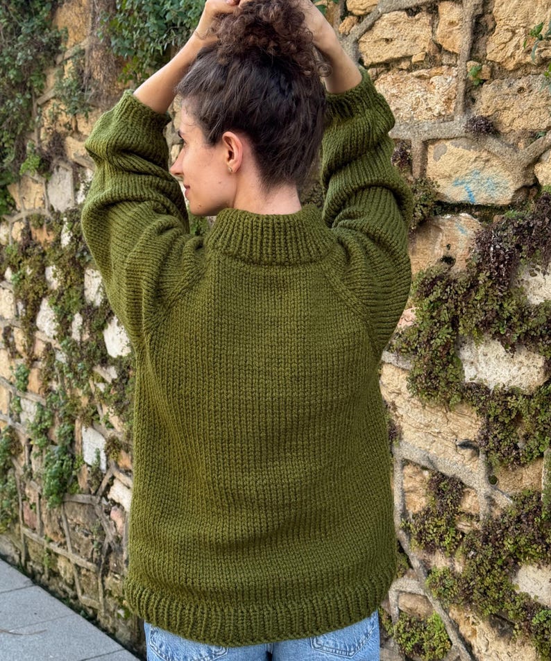 The photo shows a girl in a knitted green sweater. She is standing on a city street.