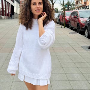 The photo shows a girl in a knitted white sweater. She is standing on a city street.