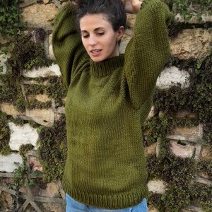 The photo shows a girl in a knitted green sweater. She is standing on a city street.