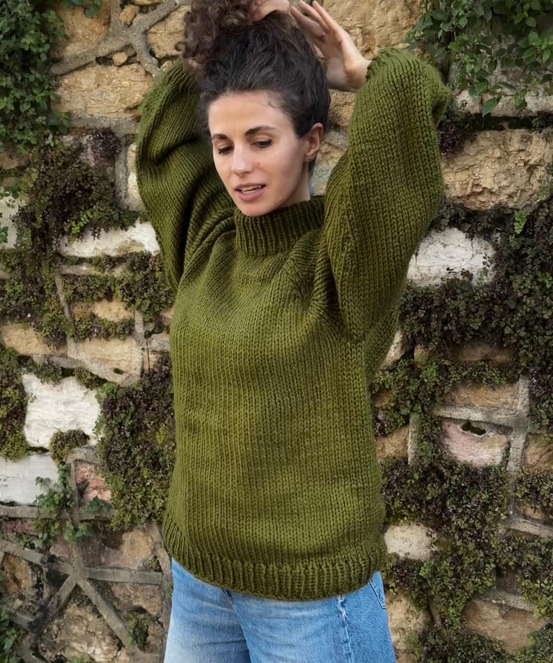 The photo shows a girl in a knitted green sweater. She is standing on a city street.