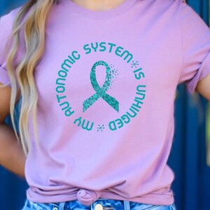 May include: A light purple t-shirt with a teal ribbon and the text "My Autonomic System is Unhinged" in a circle.