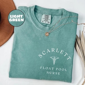 Może przedstawiać: Jasnozielony T-shirt z napisem "SCARLETT FLOAT POOL NURSE" w kolorze białym. Biały symbol kaduceusza znajduje się między słowami "FLOAT" i "POOL".