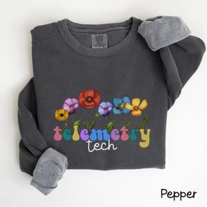 May include: A dark gray sweatshirt with a colorful flower design and the text "telemetry tech" in rainbow letters.