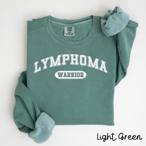May include: Light green sweatshirt with the text "Lymphoma Warrior" in white.