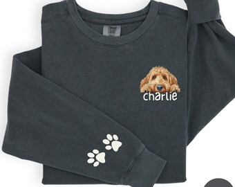 May include: Pepper-colored long-sleeve sweatshirt featuring a graphic of a golden doodle dog with the name "charlie" below. Two white paw prints are on the left sleeve. The sweatshirt is made by Comfort Colors.
