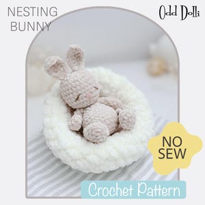 Puede incluir: Un conejito de ganchillo marrón claro en una cama blanca y suave. El conejito tiene orejas largas y ojos cerrados. La imagen incluye el texto "NESTING BUNNY", "NO SEW" y "Crochet Pattern".