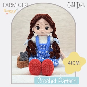 Puede incluir: Muñeca de ganchillo hecha a mano, de aproximadamente 41 cm de altura, vestida con un vestido azul y blanco y zapatos rojos. La muñeca tiene el pelo castaño en trenzas y sostiene una pequeña cesta. El texto "Farm Girl Raggy" y "Crochet Pattern" son visibles.