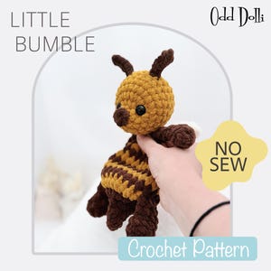 May include: Crochet pattern for a no-sew amigurumi bee toy. The bee is brown and yellow with black eyes and a brown nose. The pattern is called "Little Bumble".