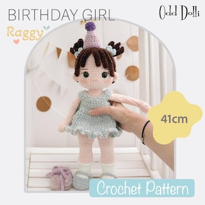 Peut inclure: Une poupée au crochet faite à la main, d'environ 41 cm de haut, avec des cheveux bruns, portant une robe bleu clair et un chapeau de fête. La poupée a une expression douce et tient un petit cadeau. Le texte "Birthday Girl Raggy" et "Crochet Pattern" sont visibles.