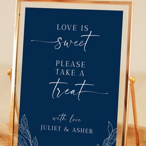 May include: A navy blue sign in a gold frame with the text "Love is sweet. Please take a treat. With love, Juliet & Asher". The sign is decorated with white leaf illustrations.