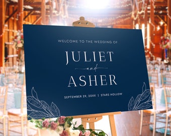 May include: A navy blue wedding welcome sign with white text that reads "Welcome to the wedding of Juliet and Asher, September 29, 20XX | Stars Hollow". The sign is on an easel in front of a rustic barn setting.