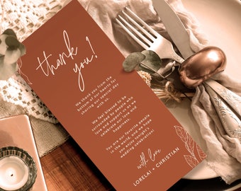 May include: A thank you card with a brown background and white text. The card says "thank you!" and includes a message expressing gratitude to guests for attending a wedding celebration. The card is decorated with white and brown floral illustrations and the names "Lorelai + Christian" at the bottom.