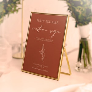 May include: A gold-framed sign with a rust-colored background and white text that reads "FULLY EDITABLE custom sign CREATE YOUR OWN CUSTOM SIGN WITH YOUR DETAILS MULTIPLE SIZE OPTIONS 5x7 & 8x10 PORTRAIT AND LANDSCAPE".