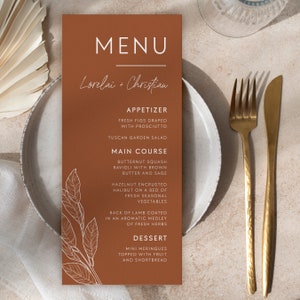 May include: A brown menu card with white text and a line drawing of a leafy branch. The menu is for a wedding reception for Lorelai and Christian. The menu includes appetizers, main courses, and desserts.