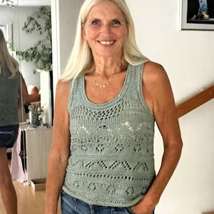 Könnte beinhalten: Ein hellgrünes Tanktop mit offenem Strickmuster, rundem Ausschnitt und aufwendigem Strickmuster. Das Oberteil wird mit Jeansshorts kombiniert. Eine Frau mit langen blonden Haaren trägt das Outfit.