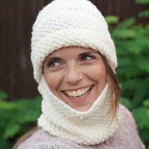 May include: A white knitted hat and neck warmer set. The hat has a slouchy fit and the neck warmer is a cowl style.