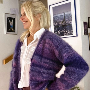 Könnte beinhalten: Eine Frau trägt einen flauschigen Cardigan mit lila und rosa Streifen und darunter ein weißes Hemd mit Knöpfen.