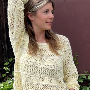 May include: A light yellow, open-weave sweater with long sleeves. The sweater features a detailed, textured pattern throughout, with a crew neck and ribbed cuffs. The garment is made of a soft, lightweight material, perfect for layering.