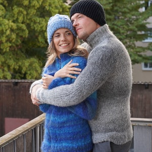 May include: A couple wearing knitted hats and jumpers, embracing each other while looking up at something in the distance.