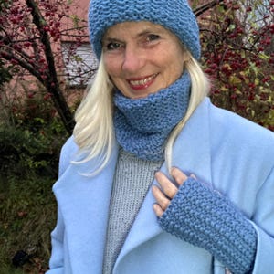 Könnte beinhalten: Ein blaues Strickset aus Mütze, Schal und Fingerlosen Handschuhen. Die Mütze ist im Slouchy-Beanie-Stil. Der Schal ist im Cowl-Neck-Stil. Die Handschuhe sind fingerlos mit einer gerippten Textur.